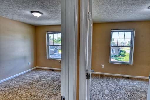A room with a carpeted floor and two windows.