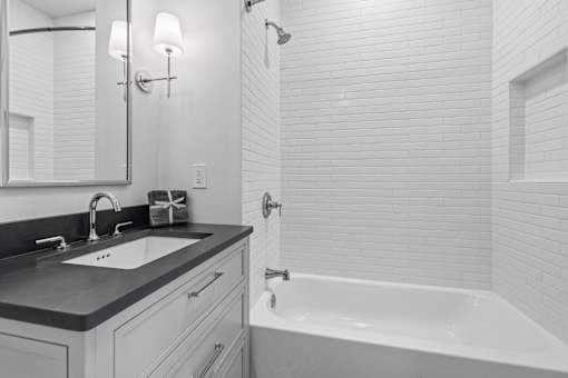 A white bathroom with a black counter top and a white bathtub.