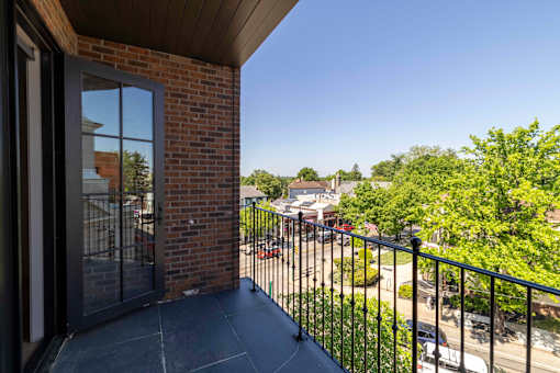 A balcony with a black railing and a view of a parking lot and trees.
