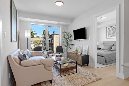 A living room with a beige couch, a coffee table, and a flat-screen TV mounted on the wall.