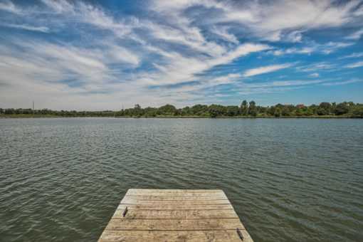 A wooden dock extends into a calm body of water under a blue sky with scattered clouds. at Standing Bear Lake, Omaha, Nebraska