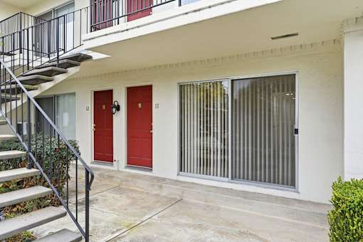 A white building with a red door and a black railing on the stairs.