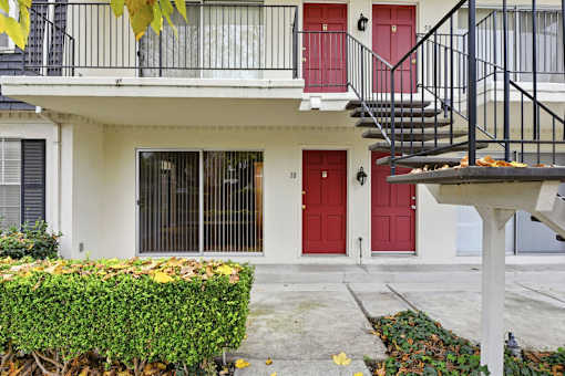 A white building with a red door and a black metal staircase.