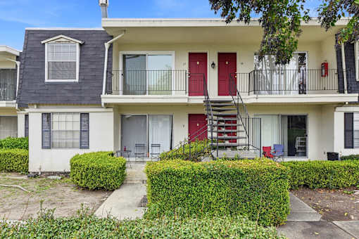 A white two-story apartment building with red doors and a red staircase.