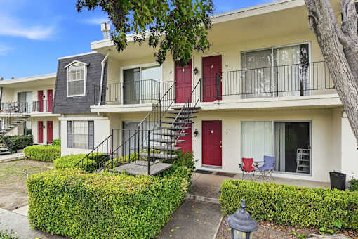 Apartment building with red doors and a tree in front.