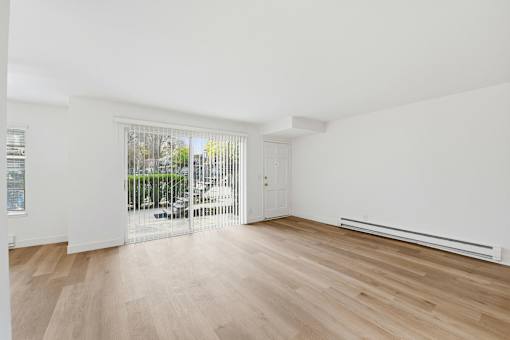 A room with wooden floors and white walls, with a view of trees through a glass door.
