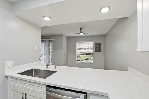 A modern kitchen with a white countertop and a stainless steel sink.