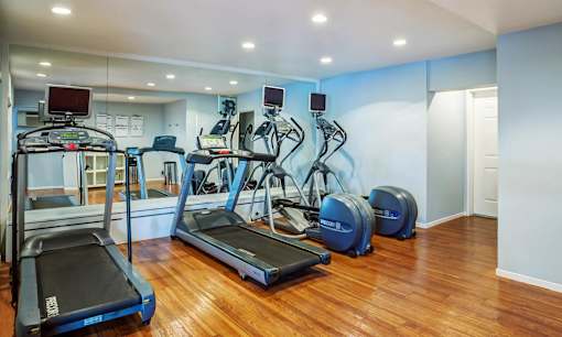 a gym with cardio equipment and mirrors in a room with wood floors