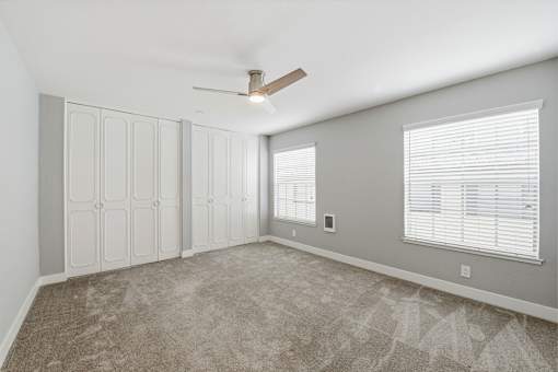 A room with a carpeted floor, a ceiling fan, and a window with blinds.