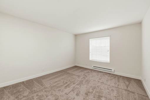 A room with a carpeted floor and a window with blinds.