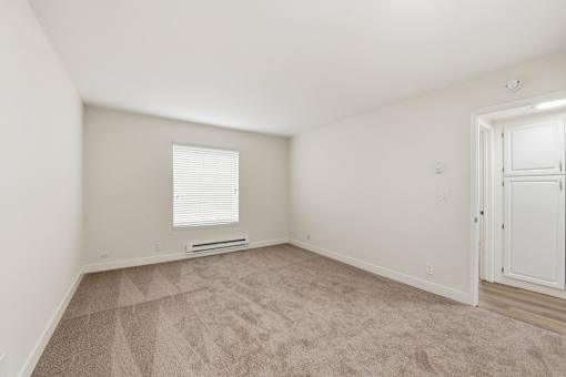 A room with a carpeted floor and a window with blinds.