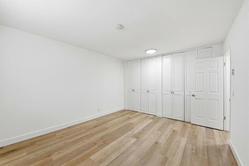 A room with white walls and wooden flooring with a row of white closets.