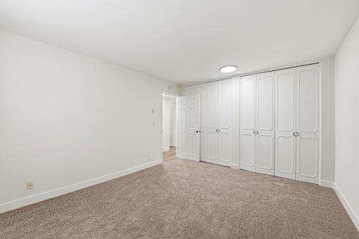 A room with white walls and a carpeted floor with a row of closets on one side.