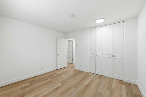 A room with white walls and wooden flooring with a door on the left and a set of white cupboards on the right.