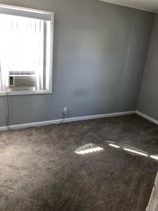 A room with a carpeted floor and a window with blinds.