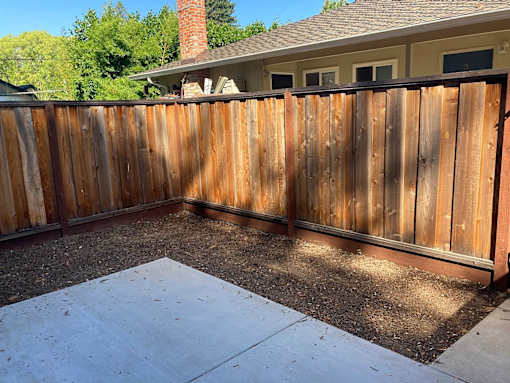 A wooden fence surrounds a concrete patio.