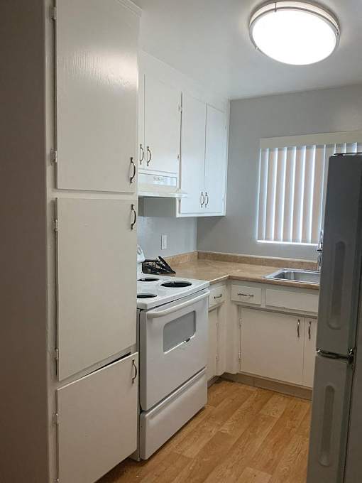 A kitchen with white appliances and wooden floors.