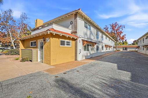 A yellow house with a red roof is in front of a white building.