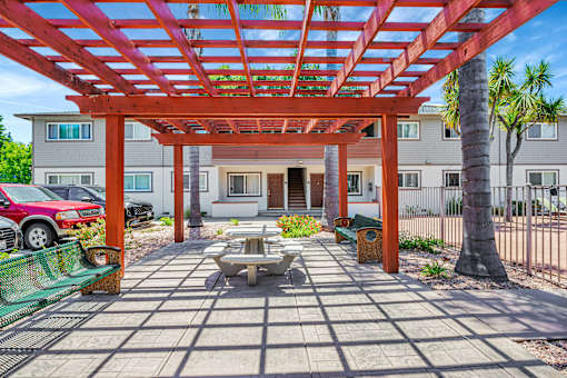 A red car is parked under a wooden pergola.