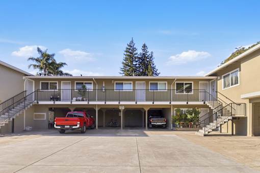 A red car is parked in the garage of a two-story apartment building.