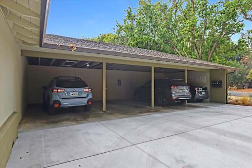 A carport with three cars parked inside.