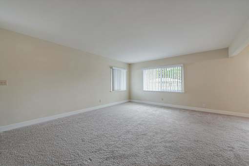A room with carpeted floor and two windows.
