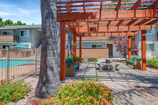 A wooden pergola is over a patio with a table and chairs.