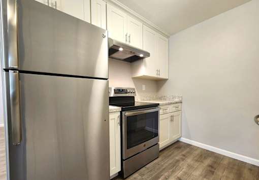 A kitchen with a stainless steel refrigerator and wooden flooring.