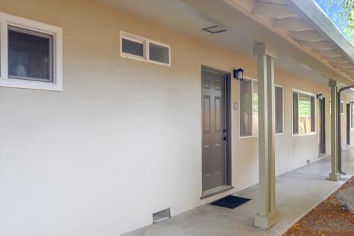 A white building with a grey door and a small window on the side.