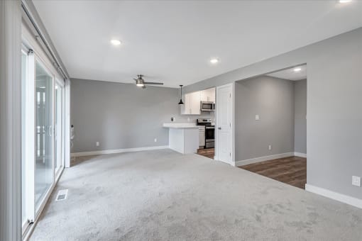 an empty living room with a kitchen in the background