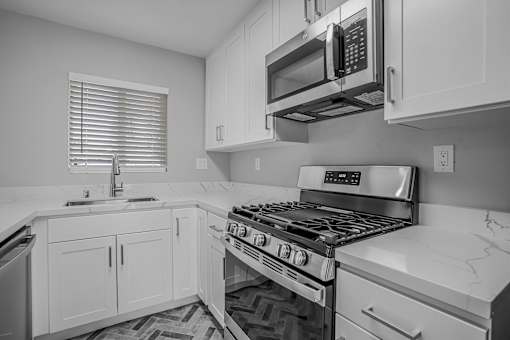 A black and white photo of a kitchen with a stove, microwave, and cabinets.