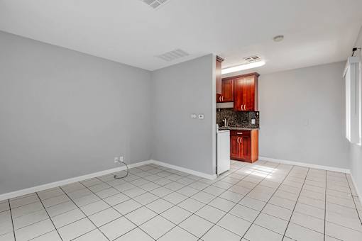 A kitchen area with white tiles on the floor and a wooden cabinet.