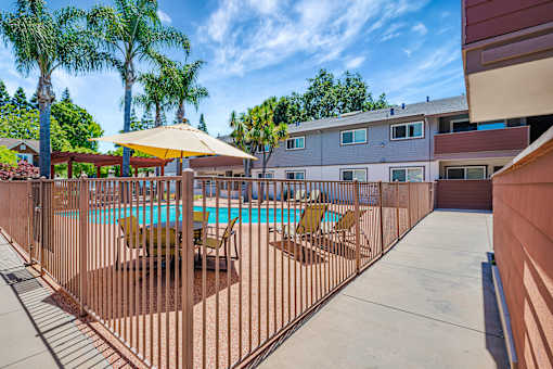 A pool surrounded by a fence with chairs and umbrellas.