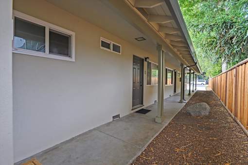 A long concrete walkway leads to a building with a white wall and a window.