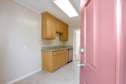 A pink door is on the right side of a kitchen with wooden cabinets and a marble countertop.