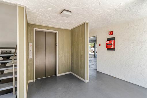 A room with a white ceiling and a grey floor with a wooden door and a red fire extinguisher on the wall.
