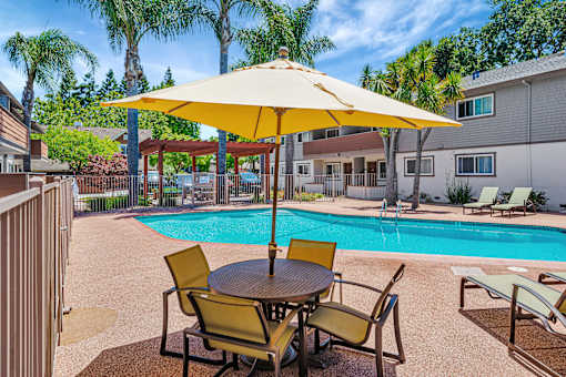 A yellow umbrella shades a table with chairs around a pool.
