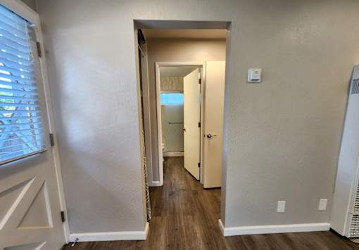 A hallway with a white door and a window with blinds on the left.