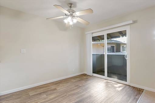 A room with a ceiling fan and sliding glass doors.