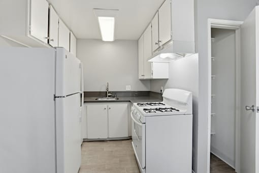 A white kitchen with a refrigerator, stove, and sink.