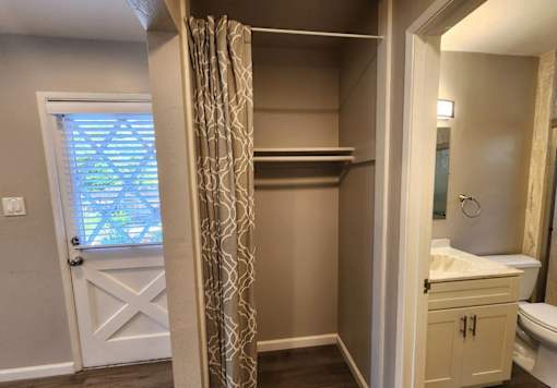 A bathroom with a white door, a window with a curtain, a sink, and a toilet.