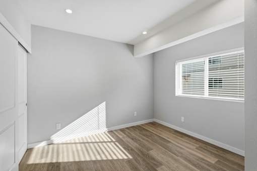 A room with a white door, a window with blinds, and a wooden floor.