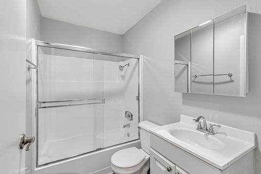 A white bathroom with a toilet, sink, and shower.