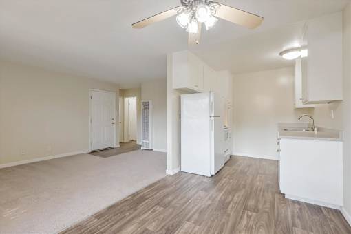A well-lit, empty living space with a kitchenette and a refrigerator.