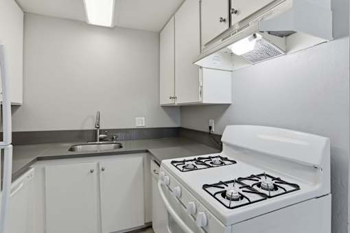 A white kitchen with a stove, sink, and cabinets.
