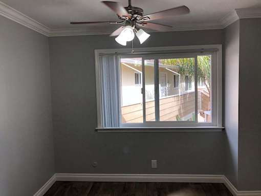 A room with a ceiling fan and a window overlooking a house.