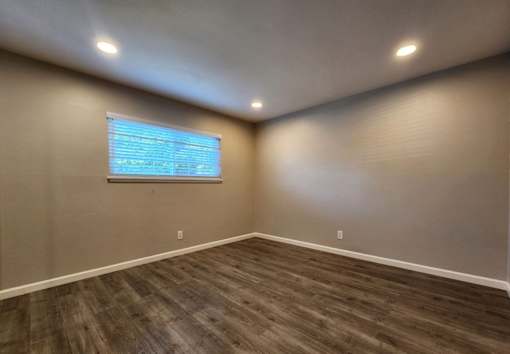 A room with wooden flooring and a window with blinds.