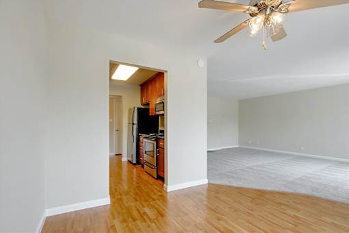 A room with a ceiling fan and a kitchen area in the background.