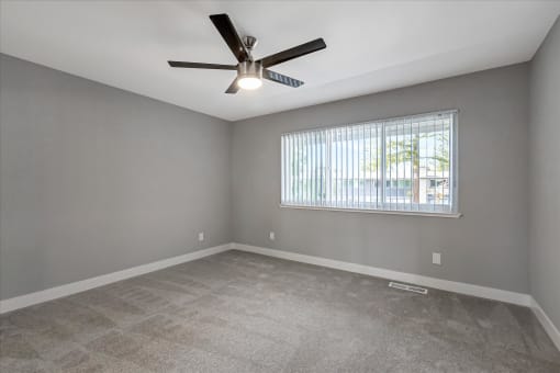 an empty living room with a ceiling fan and a window