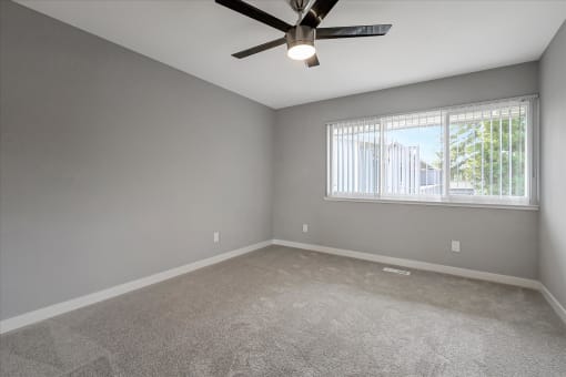 an empty living room with a ceiling fan and a window